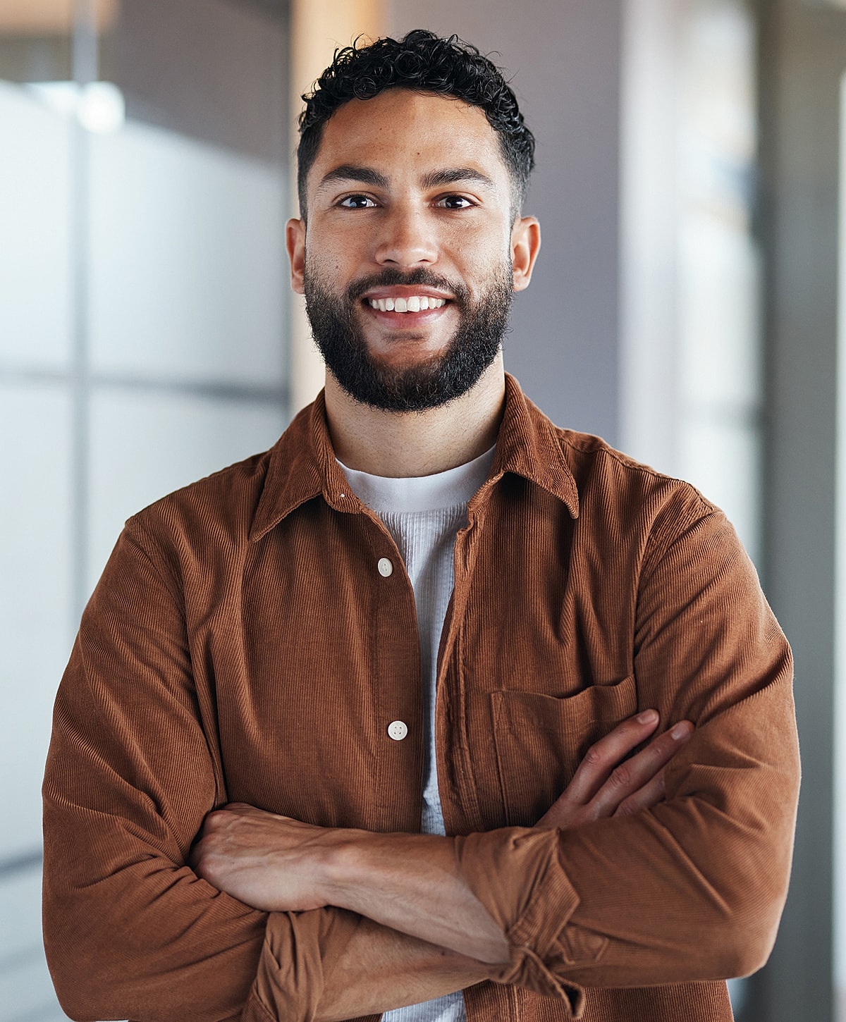 Smiling man with beard, arms crossed indoors.