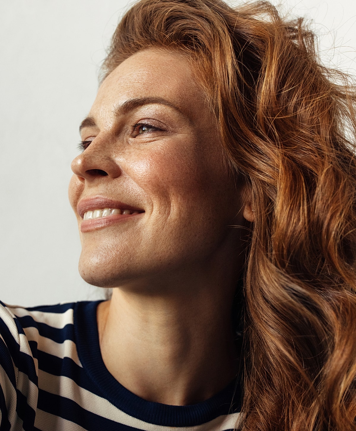 Woman smiling with long, wavy red hair.