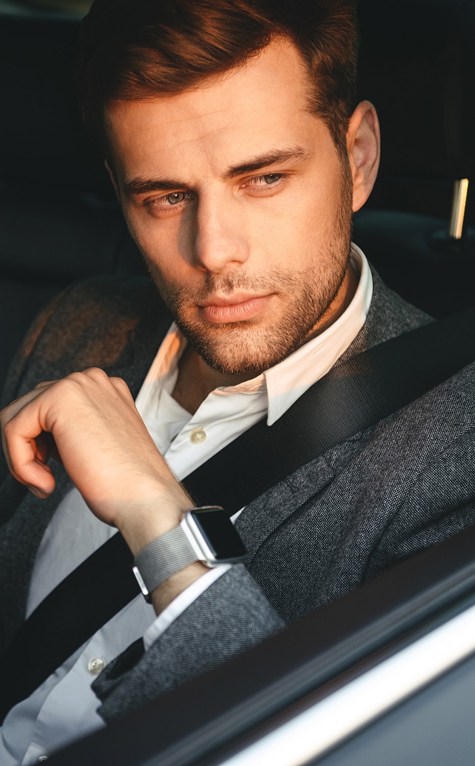 Man in car wearing a smartwatch, deep in thought.