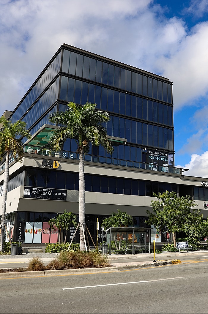 Modern office building with palm trees and signage.