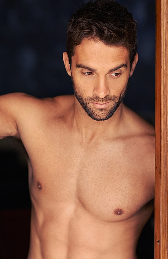 Shirtless man leaning against doorway, thoughtful expression.