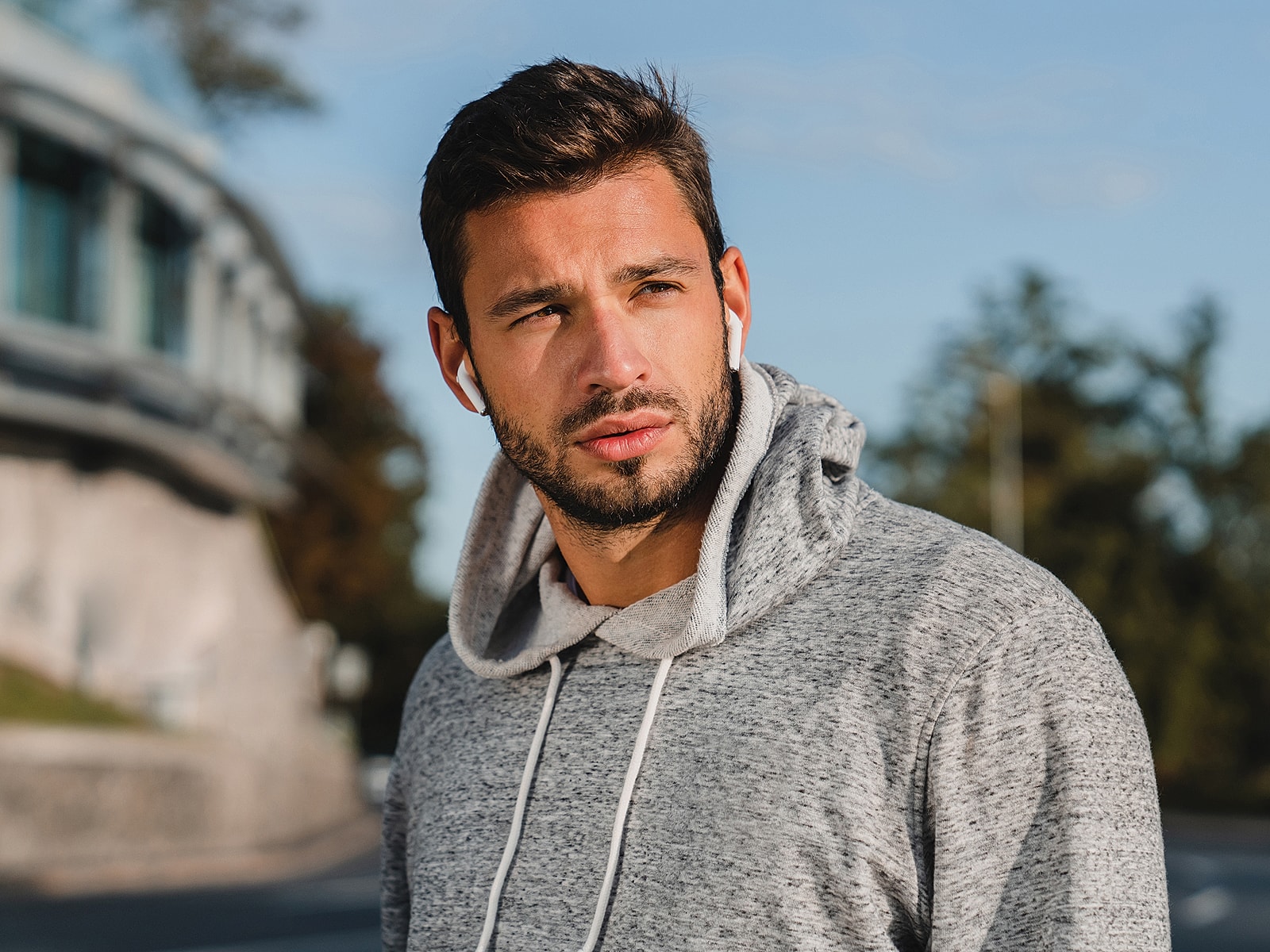 Athletic man wearing hoodie with earbuds outdoors.